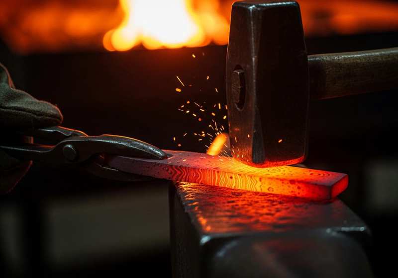 Blacksmith forging Damascus steel blade during traditional sword making process